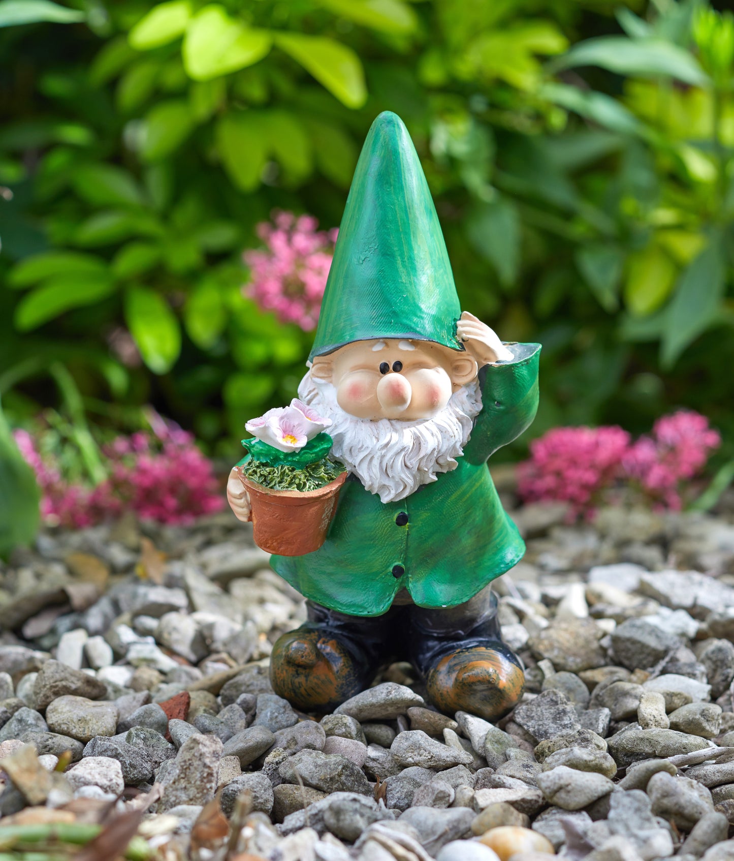Gnome figurine holding a flower pot on pebbles with greenery and pink flowers in the background