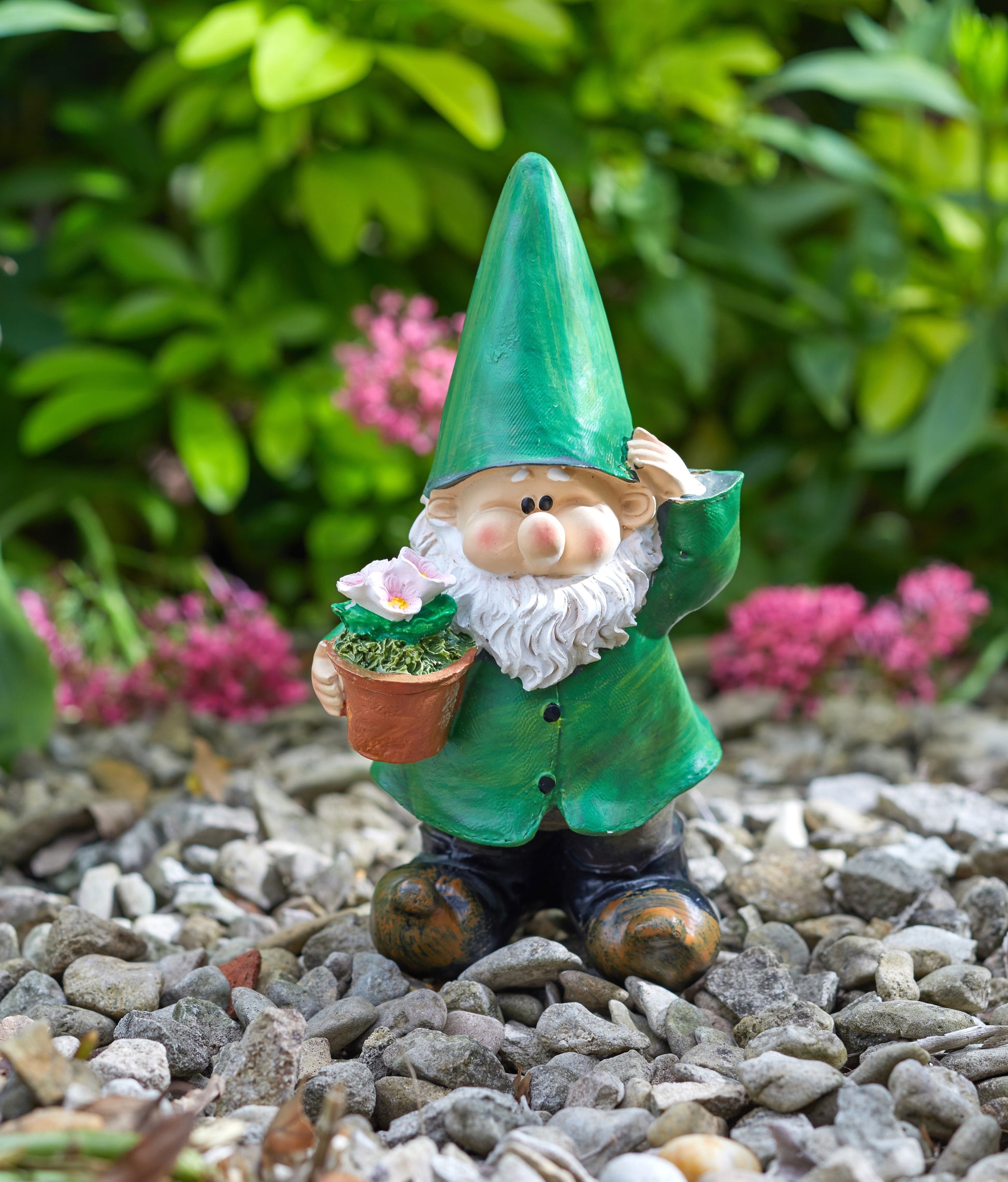 Gnome figurine holding a flower pot on pebbles with greenery and pink flowers in the background
