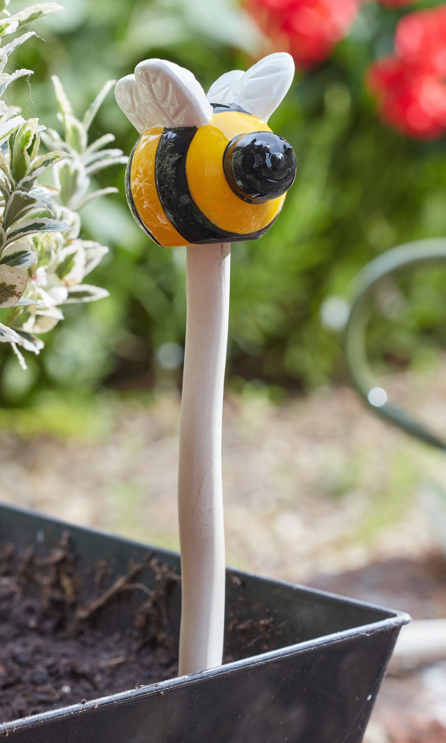 Bee-shaped plant stake in a garden setting with blurred flowers in the background