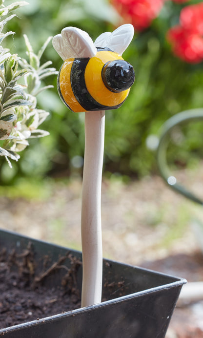 Bee-shaped plant stake in a garden setting with blurred flowers in the background