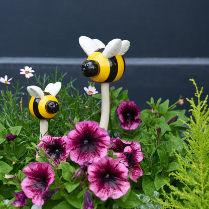 Two bee-shaped garden stakes among pink flowers with a dark background