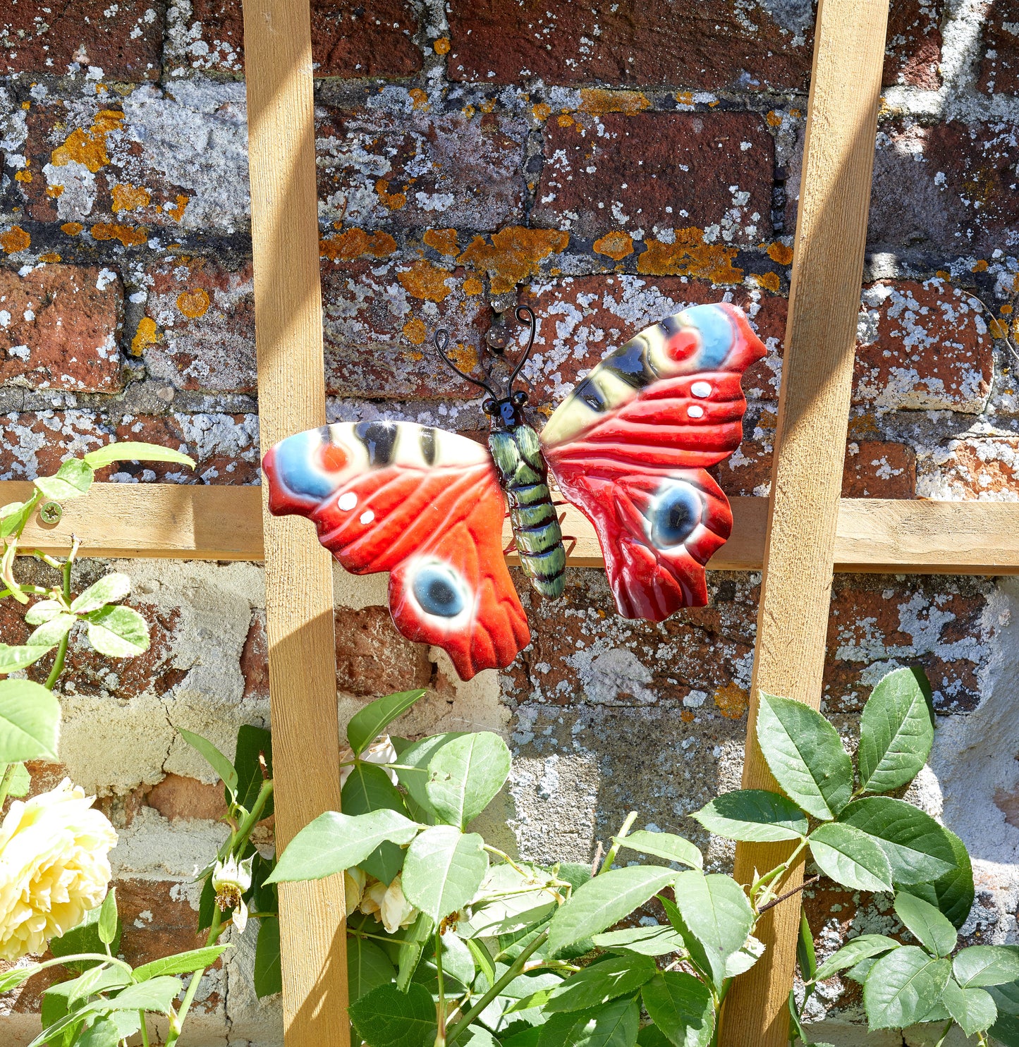 Decorative butterfly on a wooden stand with a brick wall and plants in the background