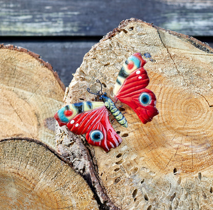 Colourful butterfly-shaped object with a small insect-like figure in the centre on a wooden log