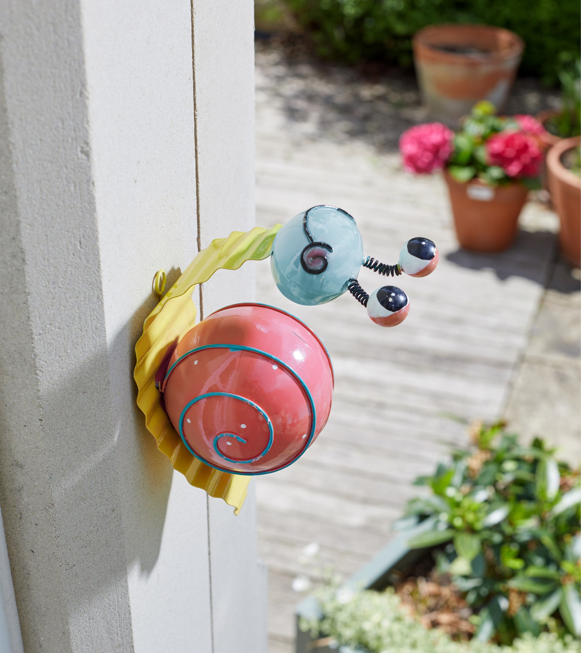 Colorful snail-shaped door hanger on a door with outdoor plants in the background