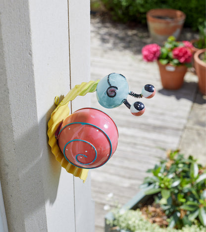 Colorful snail-shaped door hanger on a door with outdoor plants in the background