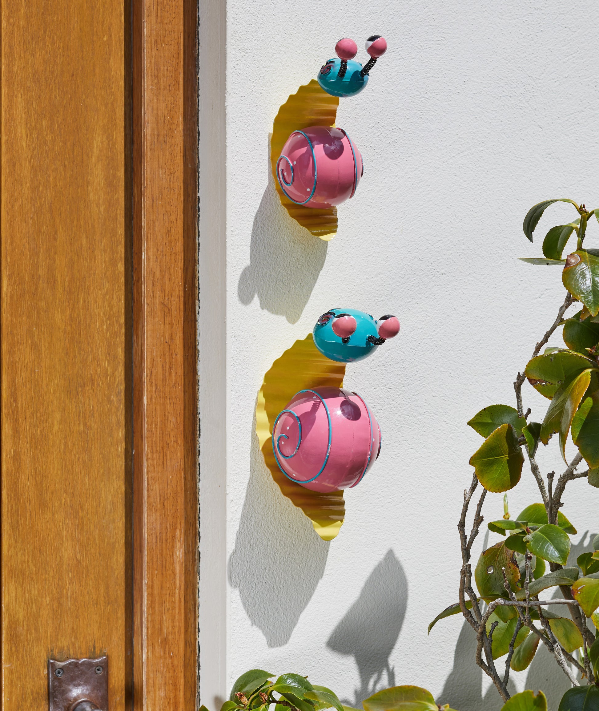 Colorful caterpillar-shaped door stopper on a wooden door with a plant in the foreground.