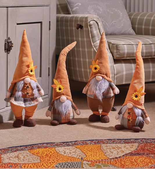 Four decorative gnomes with autumn-themed clothing in a living room setting.