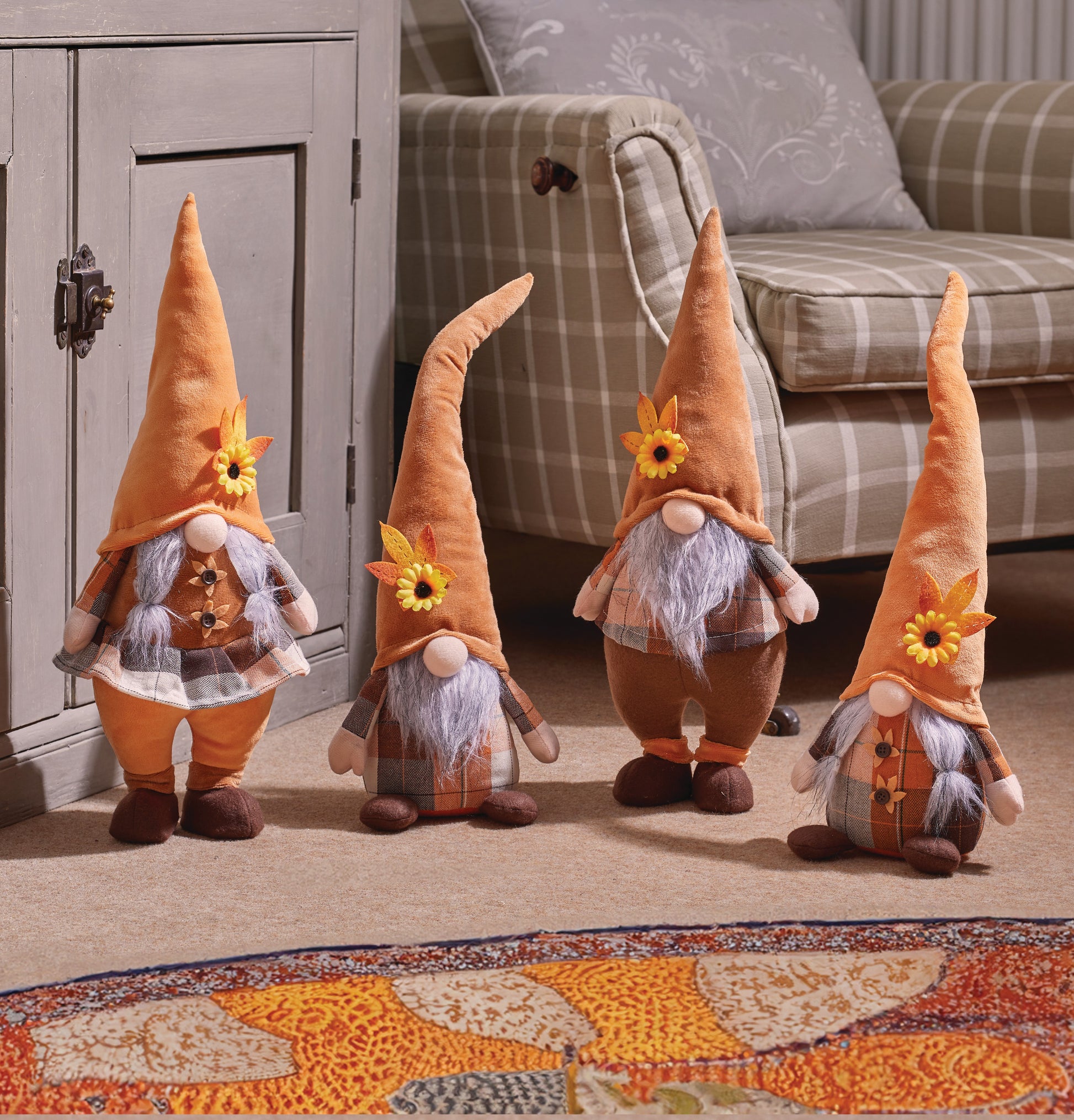 Four decorative gnomes with autumn-themed decorations on a carpeted floor.