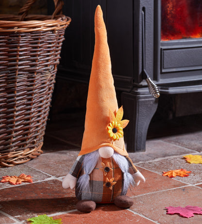Decorative gnome with an orange hat and plaid outfit in front of a fireplace.