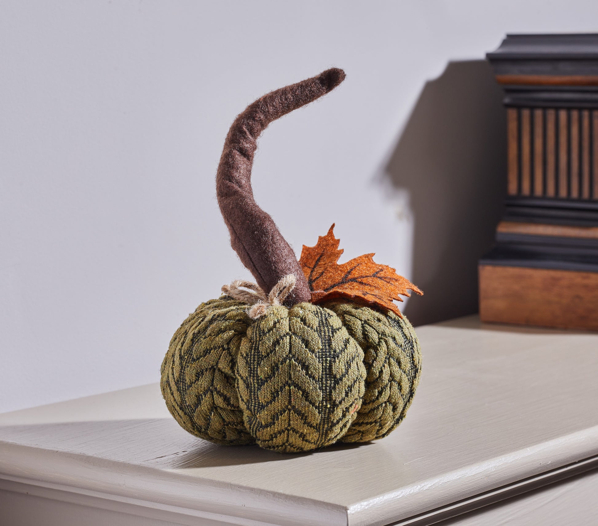 Decorative knitted pumpkin with a leaf on a surface