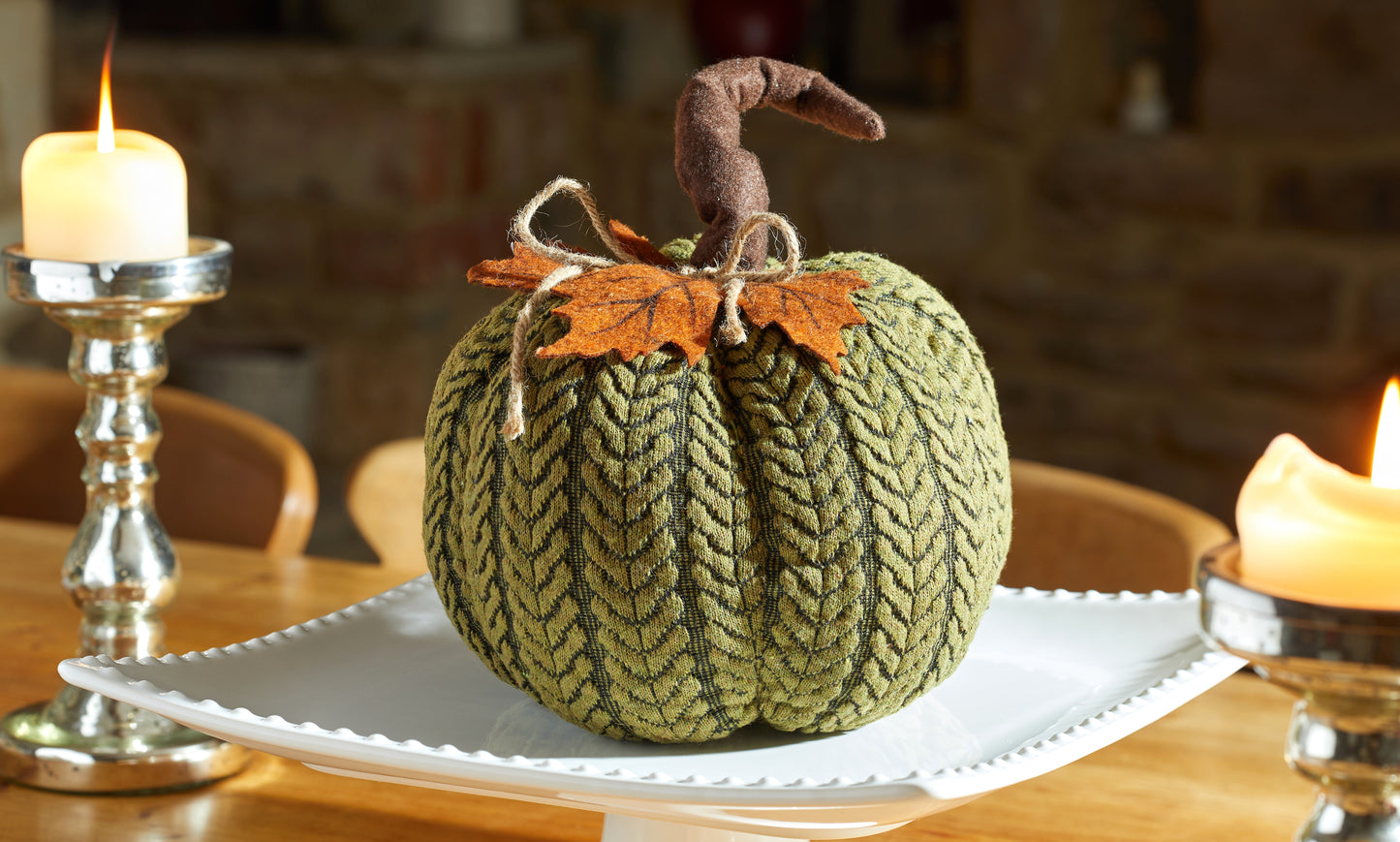 Knitted pumpkin decoration on a white plate with candles in the background