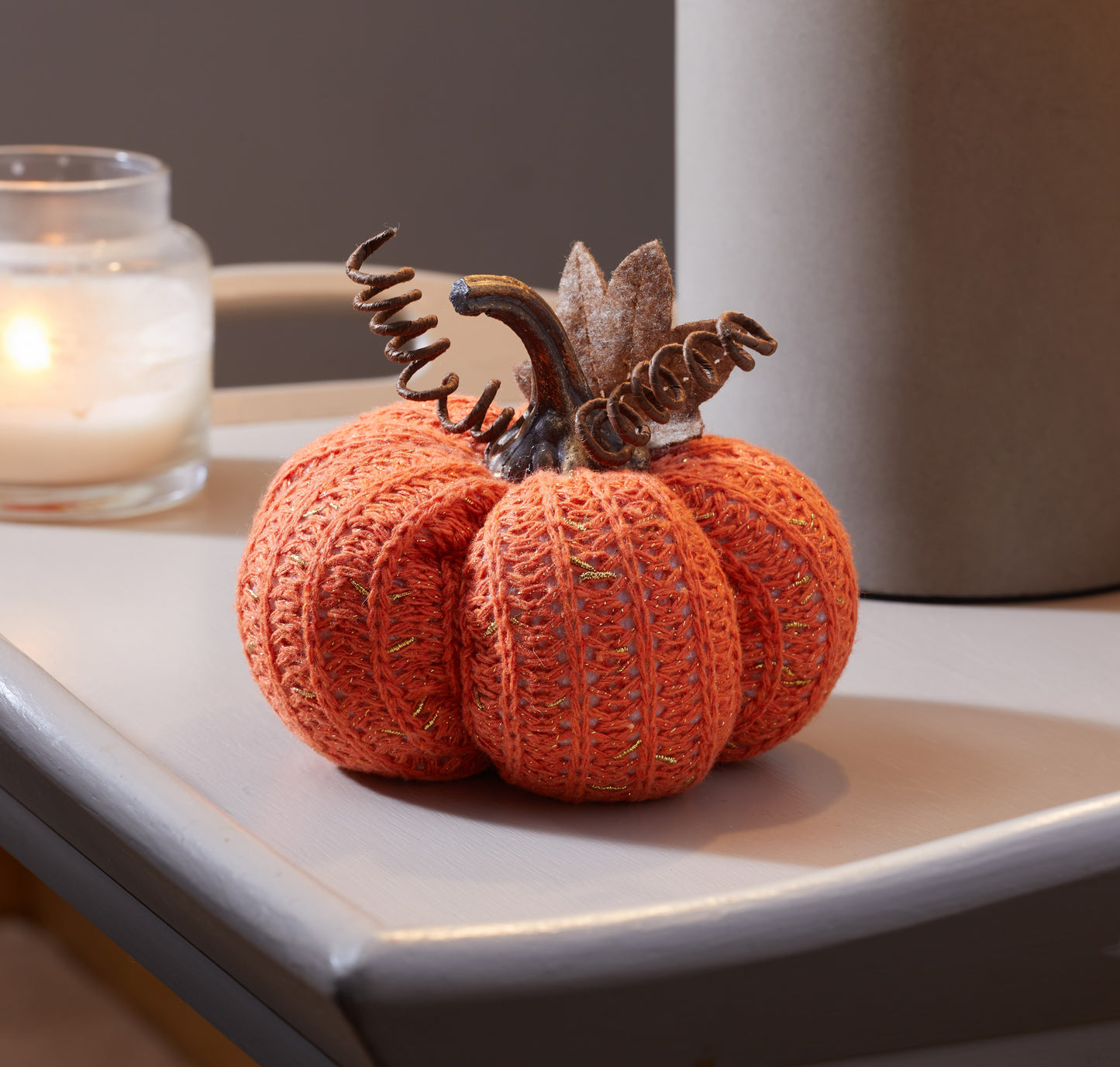 Knitted pumpkin decoration on a surface with a blurred candle in the background