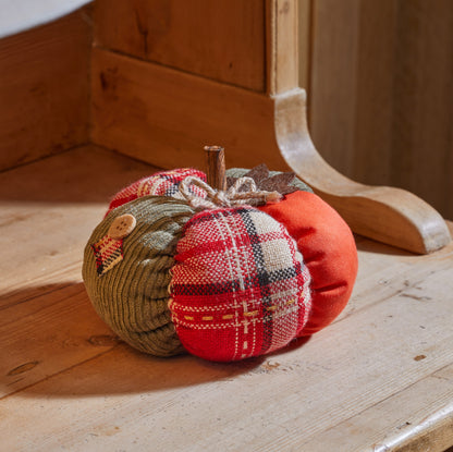 Three fabric pumpkins in plaid and solid colors on a wooden surface.