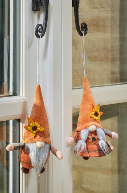 Two small gnome figurines with orange hats and sunflower decorations hanging on a door.