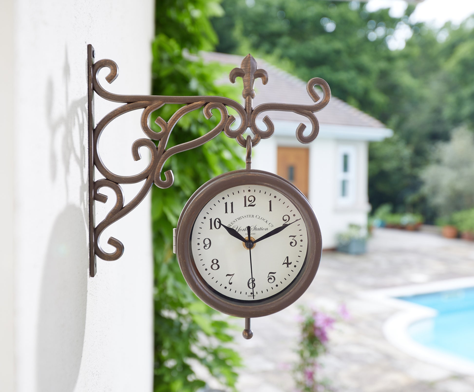 Decorative outdoor clock with garden and house in the background
