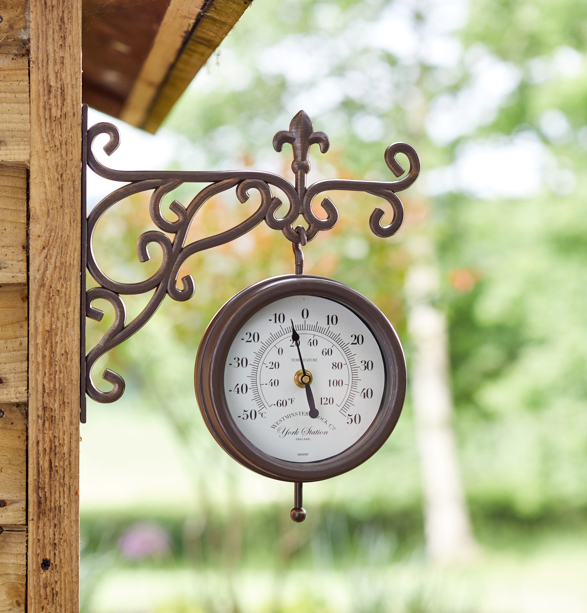 Decorative outdoor thermometer with decorative bracket on a wooden post.