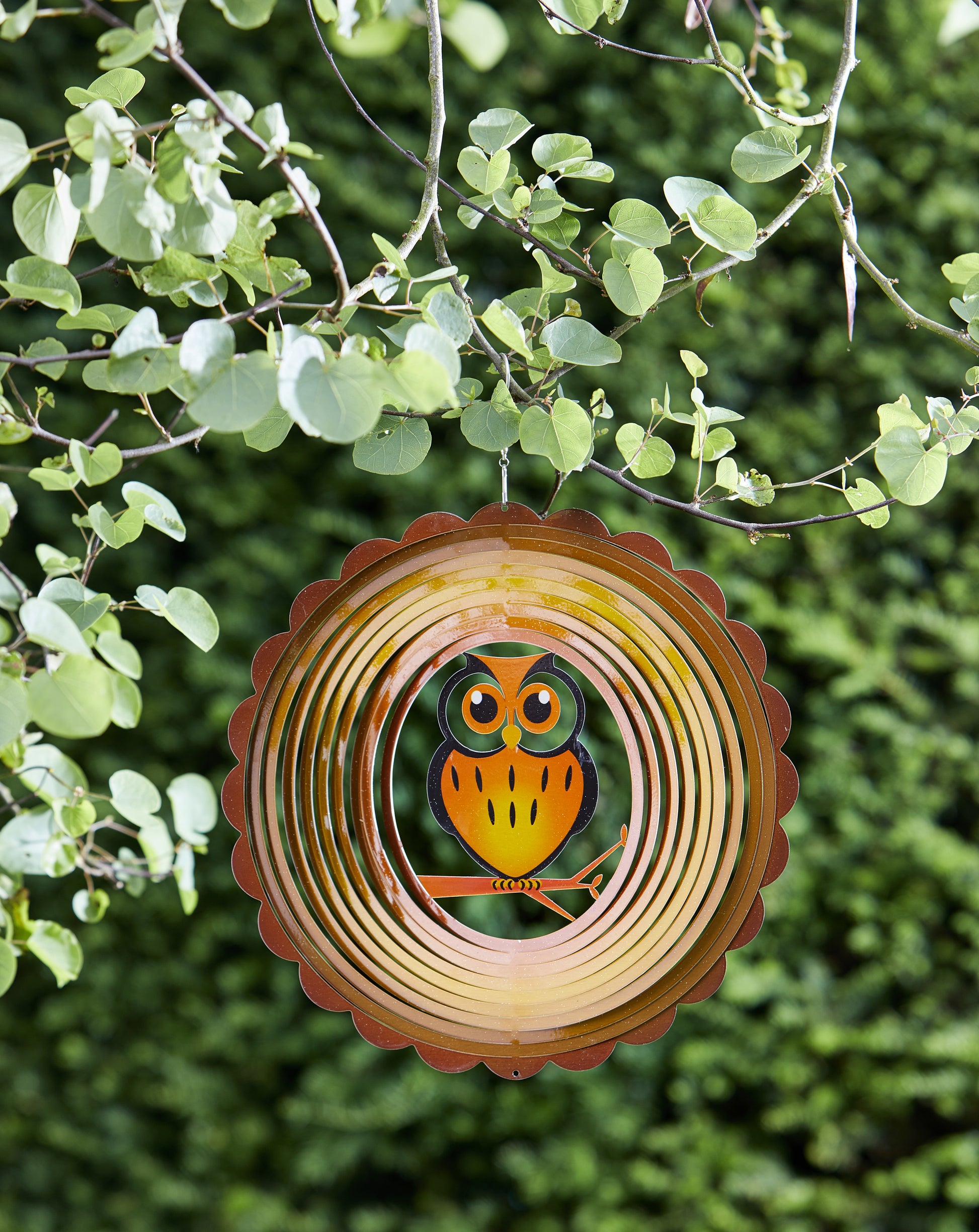 Decorative metal spiral with an owl design hanging from a tree