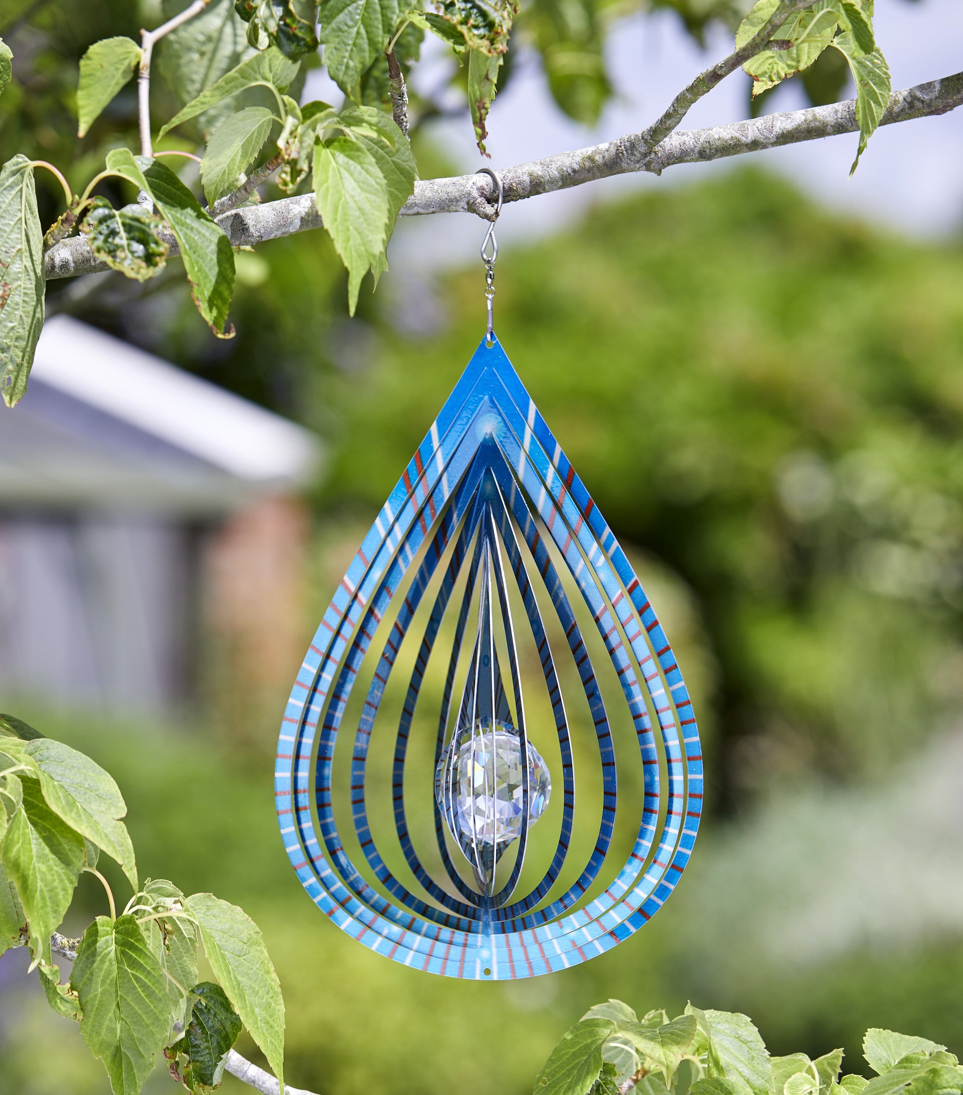 Decorative glass wind chime hanging from a tree branch with a blurred garden background