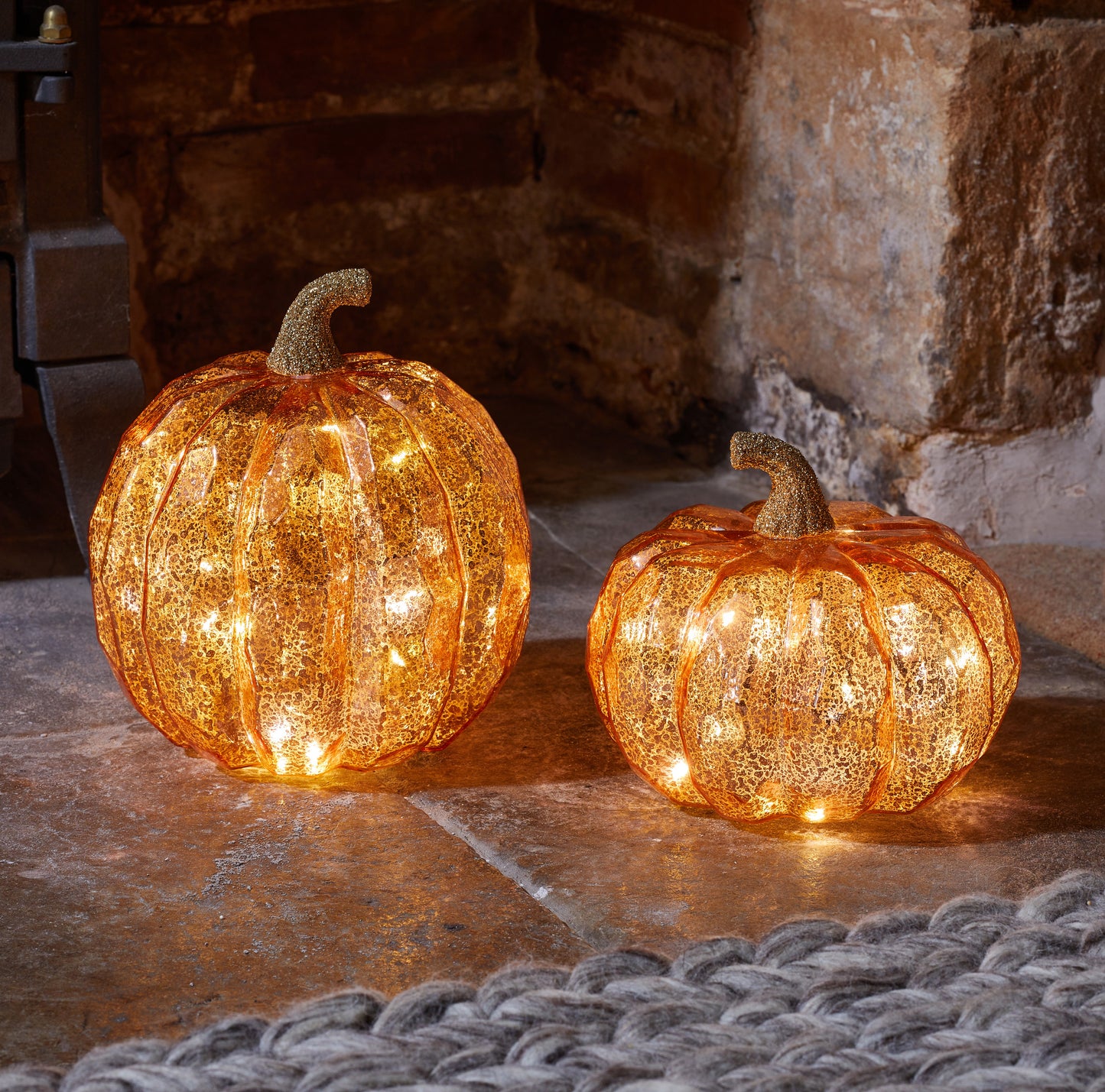 Two illuminated decorative pumpkins on a stone surface with a stone wall background.