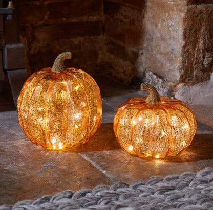 Two illuminated decorative pumpkins on a stone surface with a stone wall background.