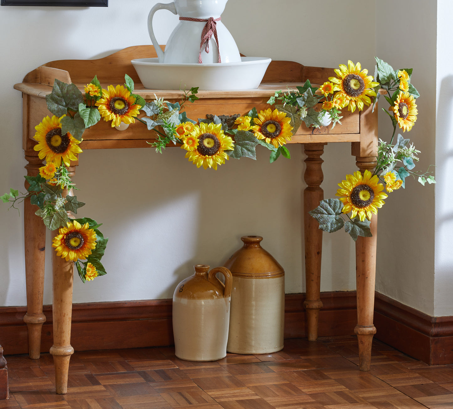 Decorative sunflower garland on a wooden table with ceramic vases underneath.