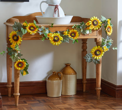 Decorative sunflower garland on a wooden table with ceramic vases underneath.