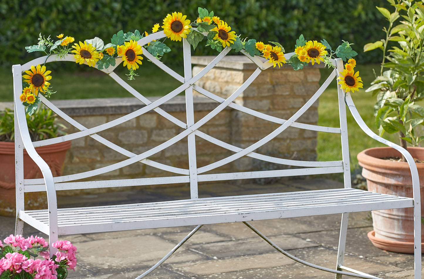 White metal bench with sunflower decorations in a garden setting