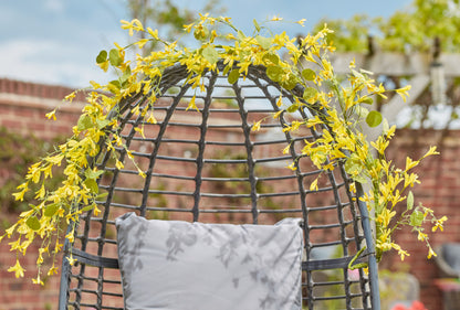 Decorative chair with yellow flowers and a gray pillow against a blurred outdoor background
