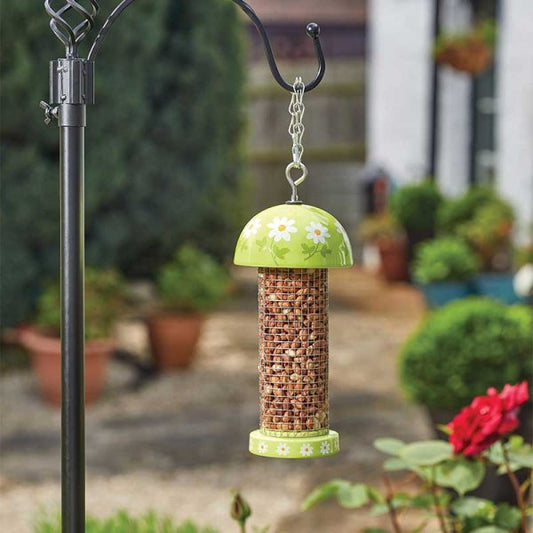 Bird feeder with green top and floral design hanging from a hook in a garden setting.