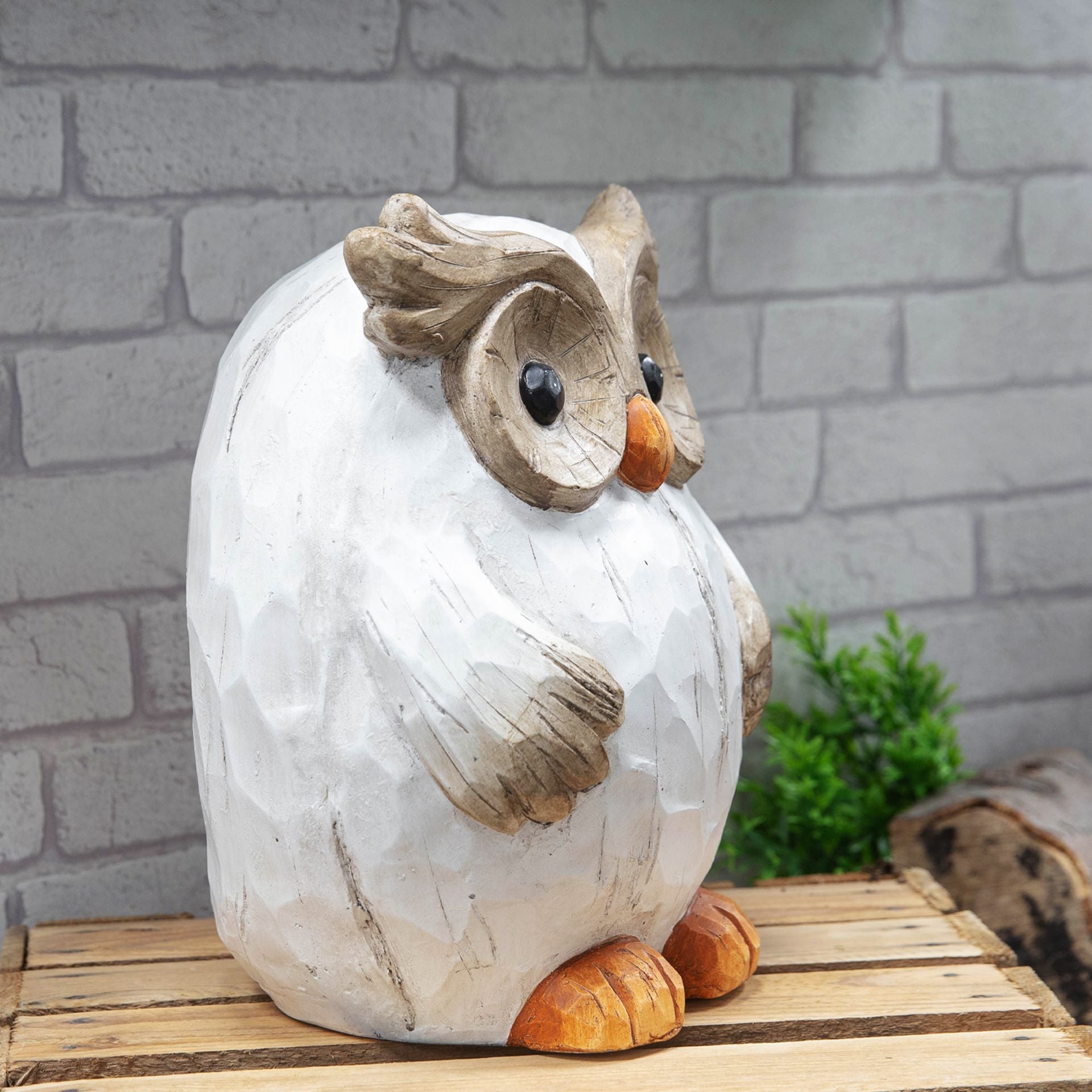Wooden owl figurine on a wooden surface with a brick wall background