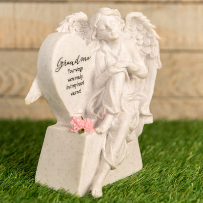 White angel statue with text and pink flower on a grassy background