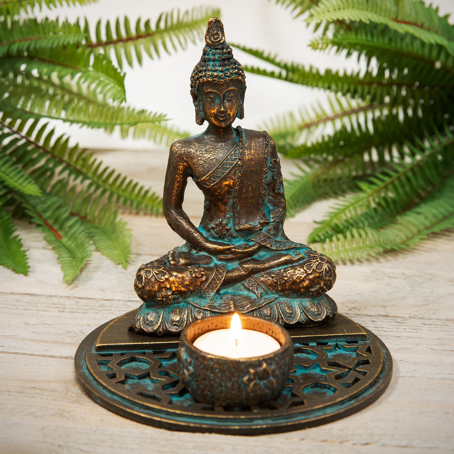 Bronze Buddha statue with a candle on a wooden surface with ferns in the background