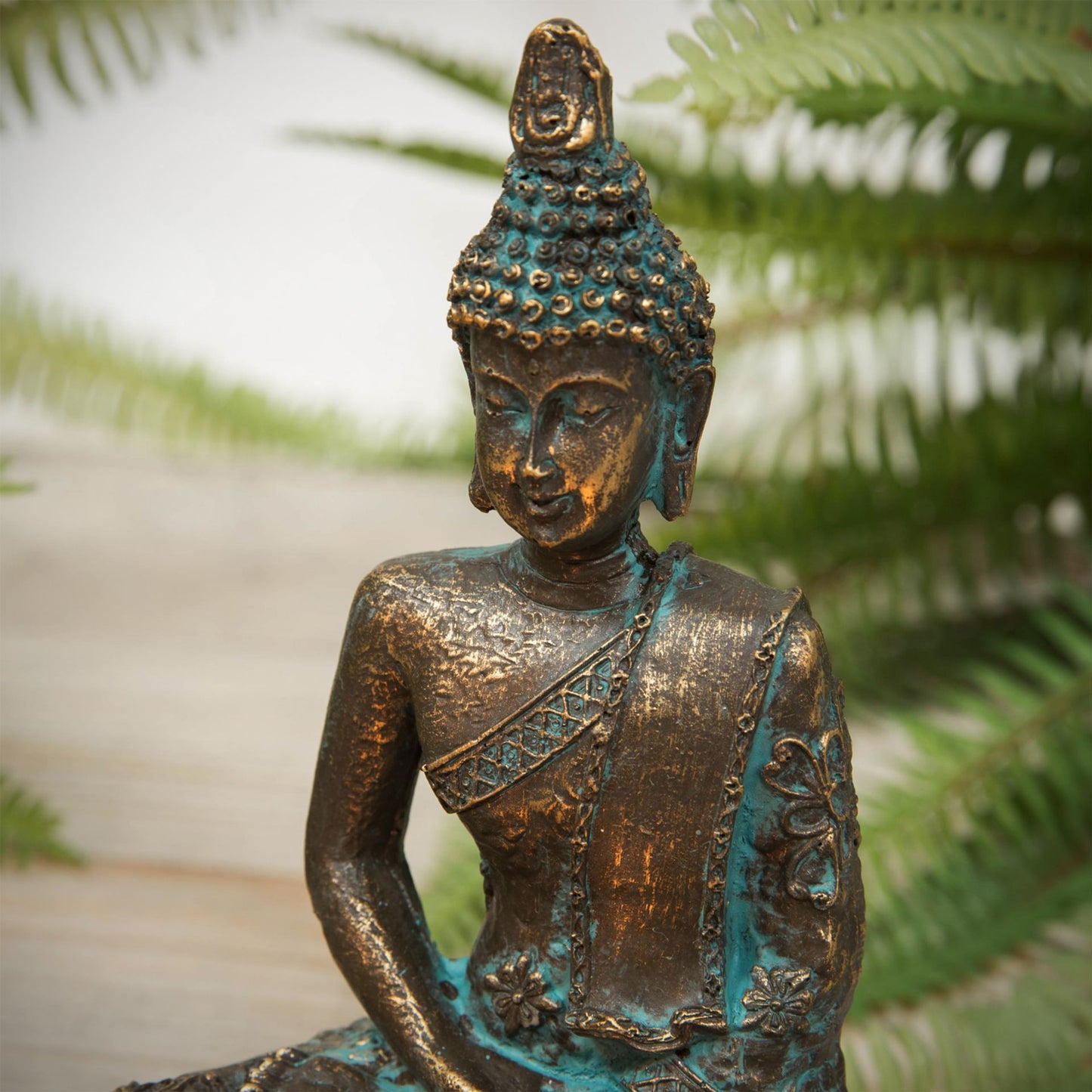 Bronze Buddha statue with green patina against a blurred natural background