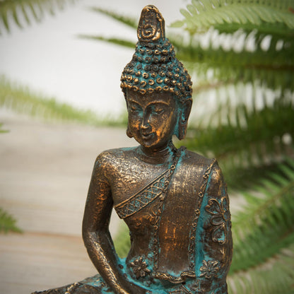 Bronze Buddha statue with green patina against a blurred natural background