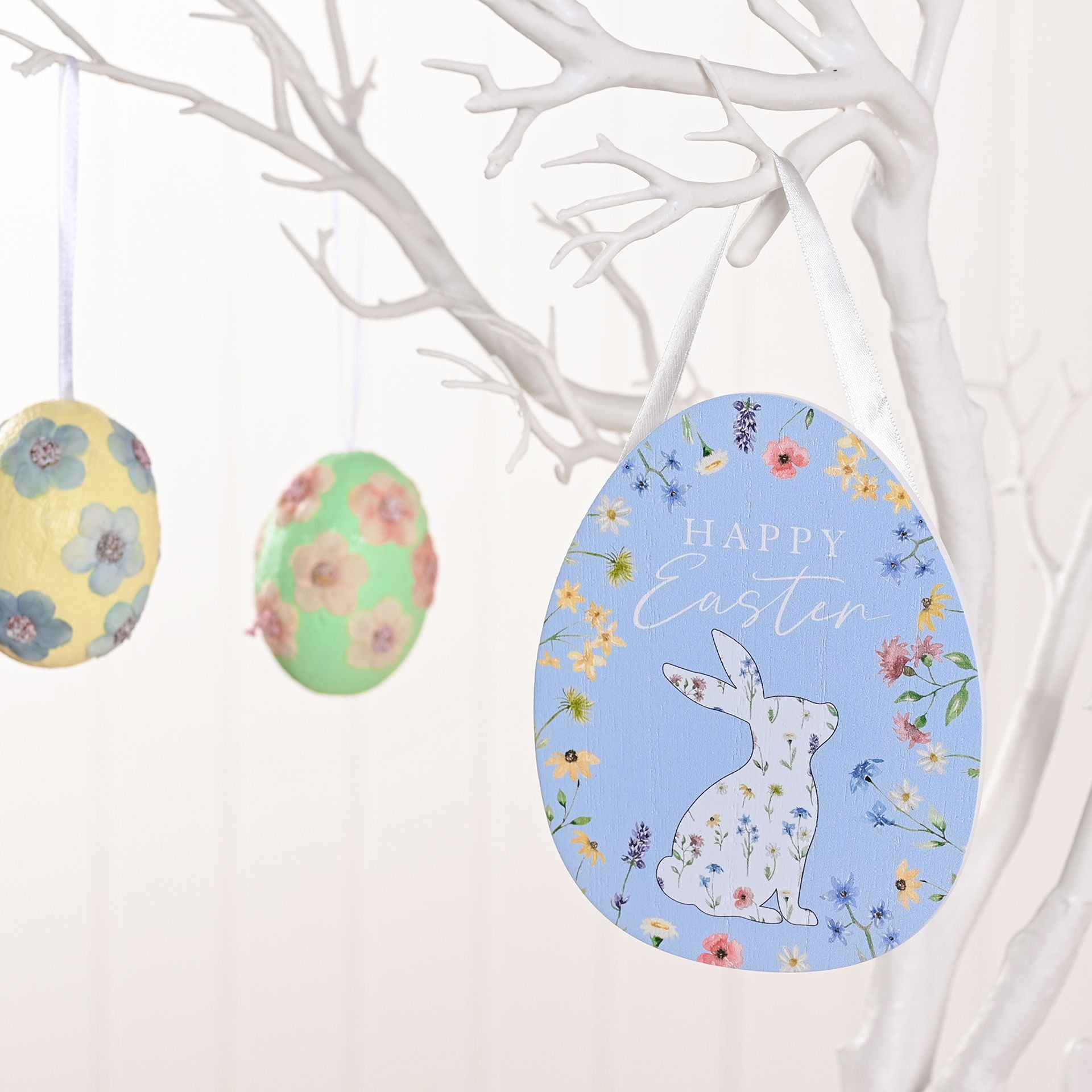 Decorative Easter eggs with floral patterns and a bunny design on a white branch background.