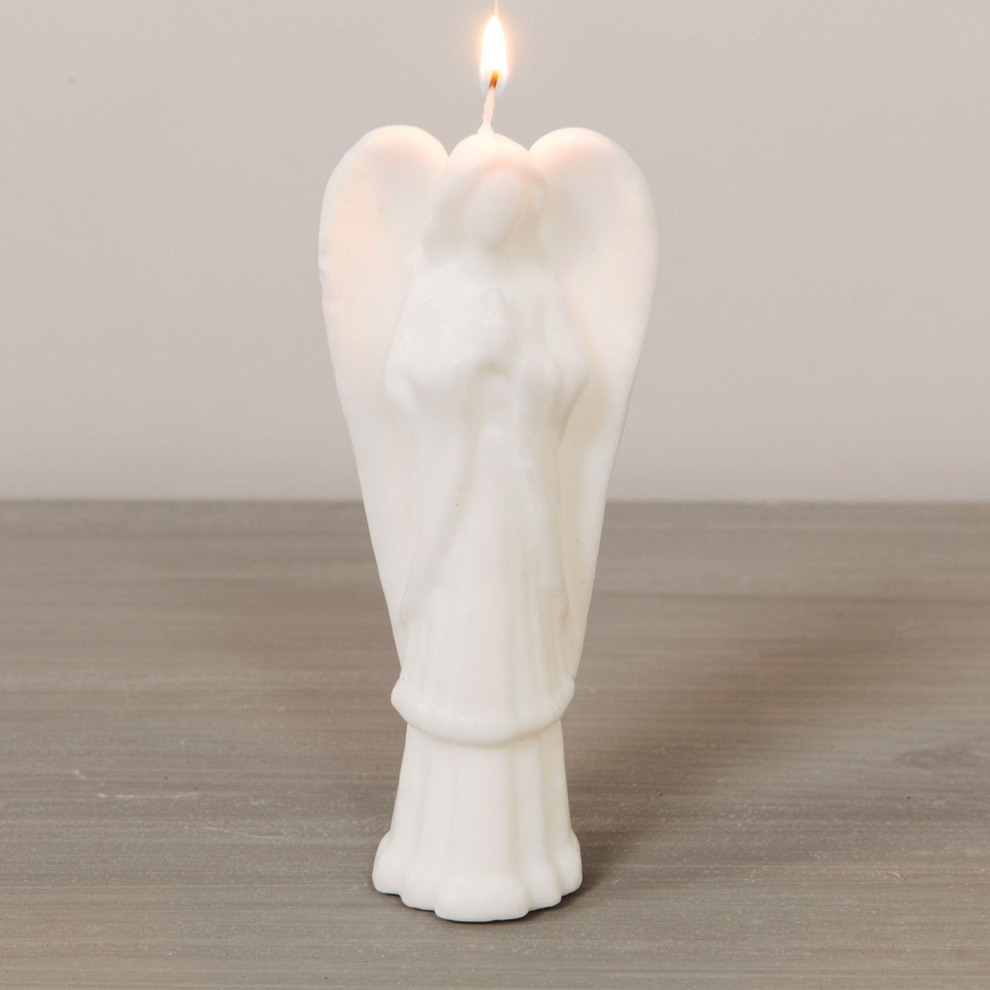 White angel-shaped candle with a lit wick on a wooden surface.