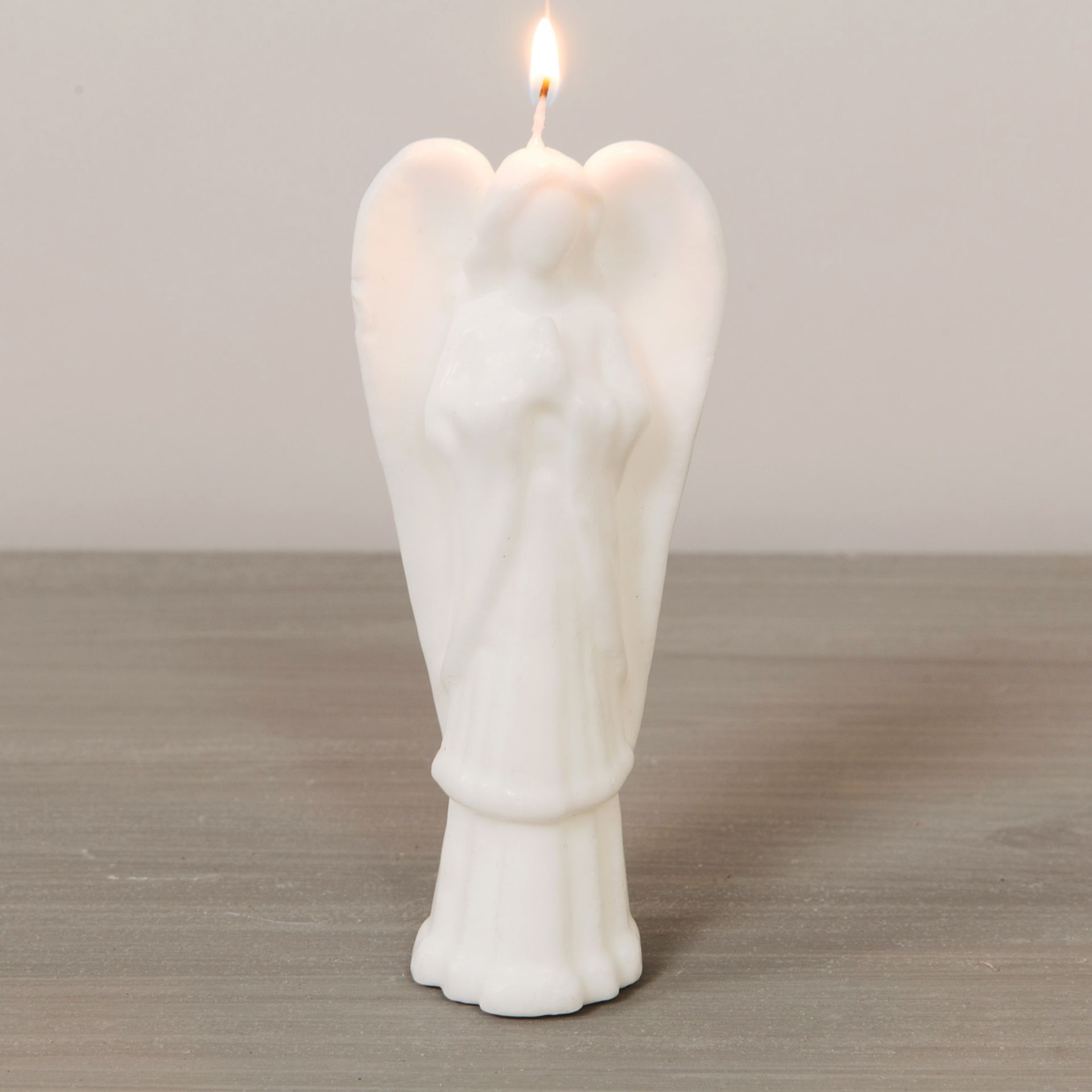 White angel-shaped candle with a lit wick on a wooden surface.