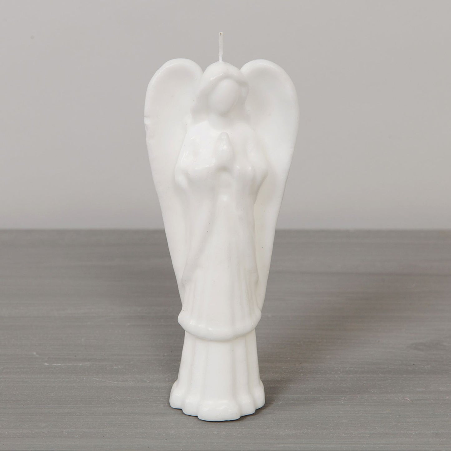 White angel-shaped candle on a gray surface with a neutral background