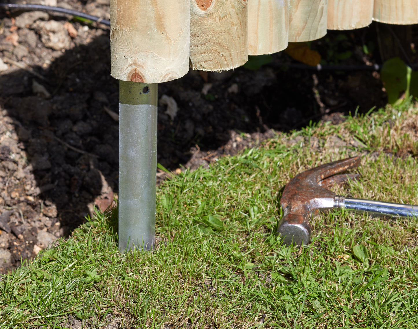 Wooden post with metal base being driven into the ground with a hammer.