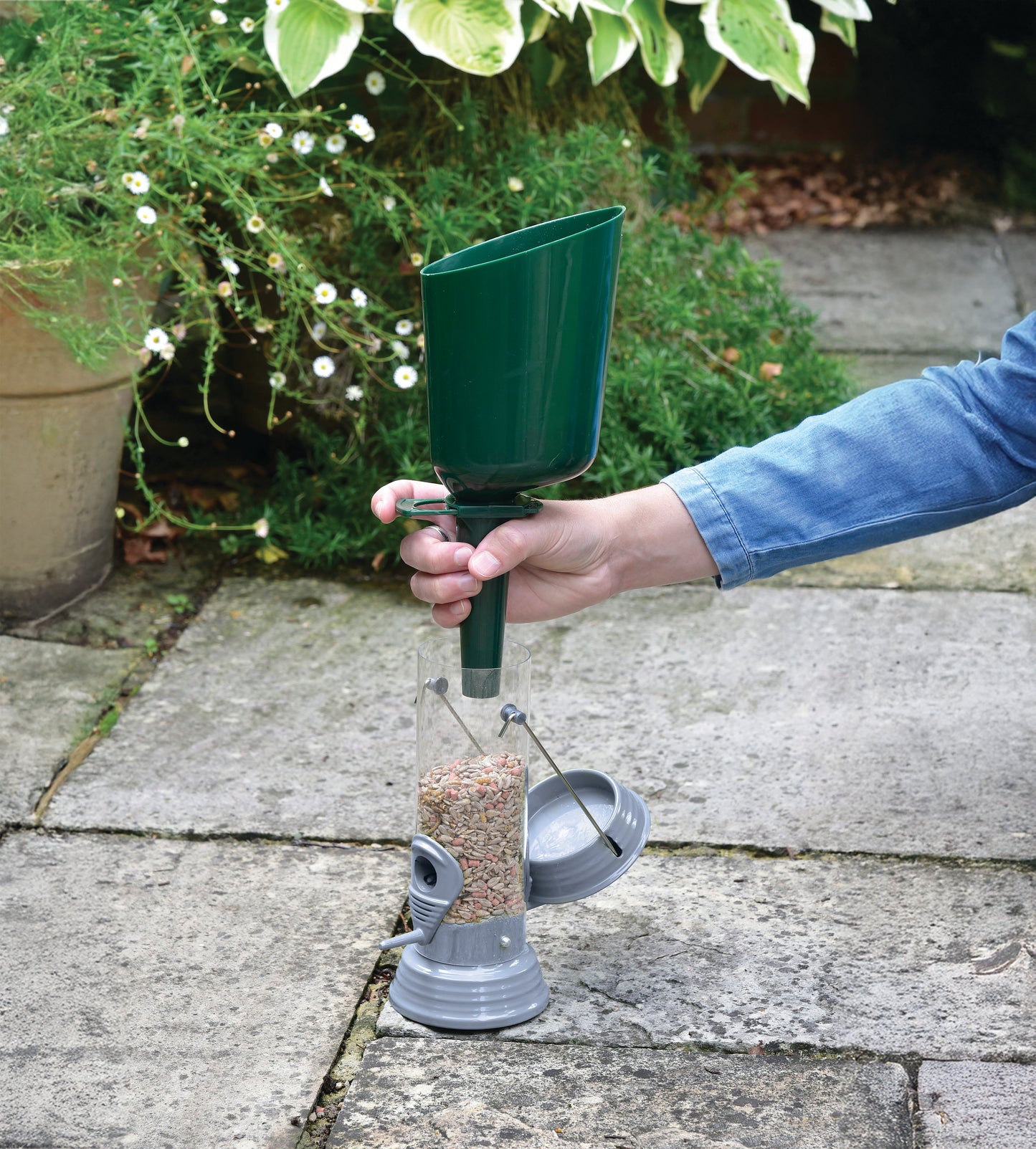 Person holding a green bird feeder on a stone patio with plants in the background