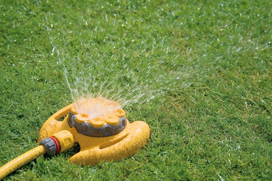 Yellow garden sprinkler spraying water on green grass
