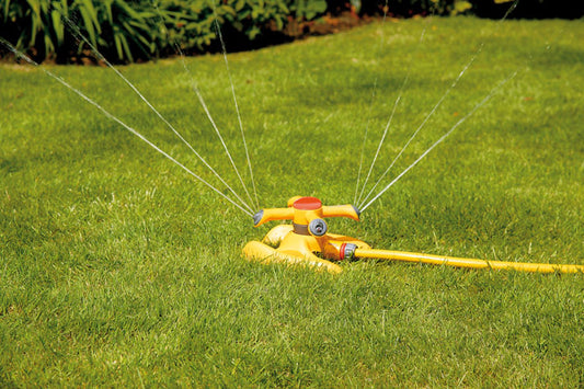 Yellow sprinkler on a grassy lawn with water spraying out