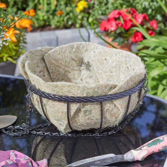 Textured woven basket with metal rim on a reflective surface with flowers in the background