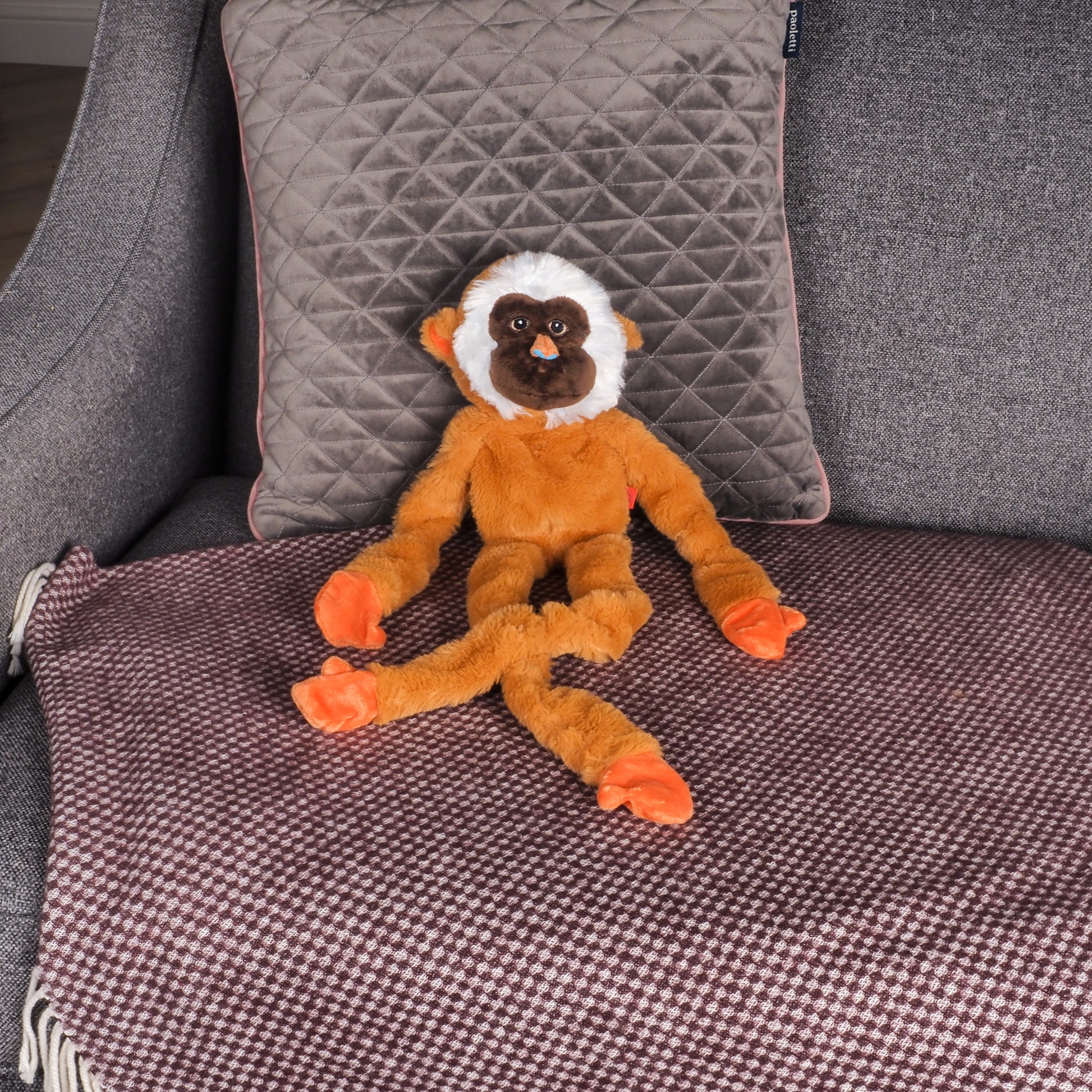 Plush monkey toy on a textured surface with pillows in the background