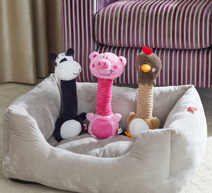 Three plush dog toys shaped like a zebra, pig, and monkey on a pet bed with a striped couch in the background.