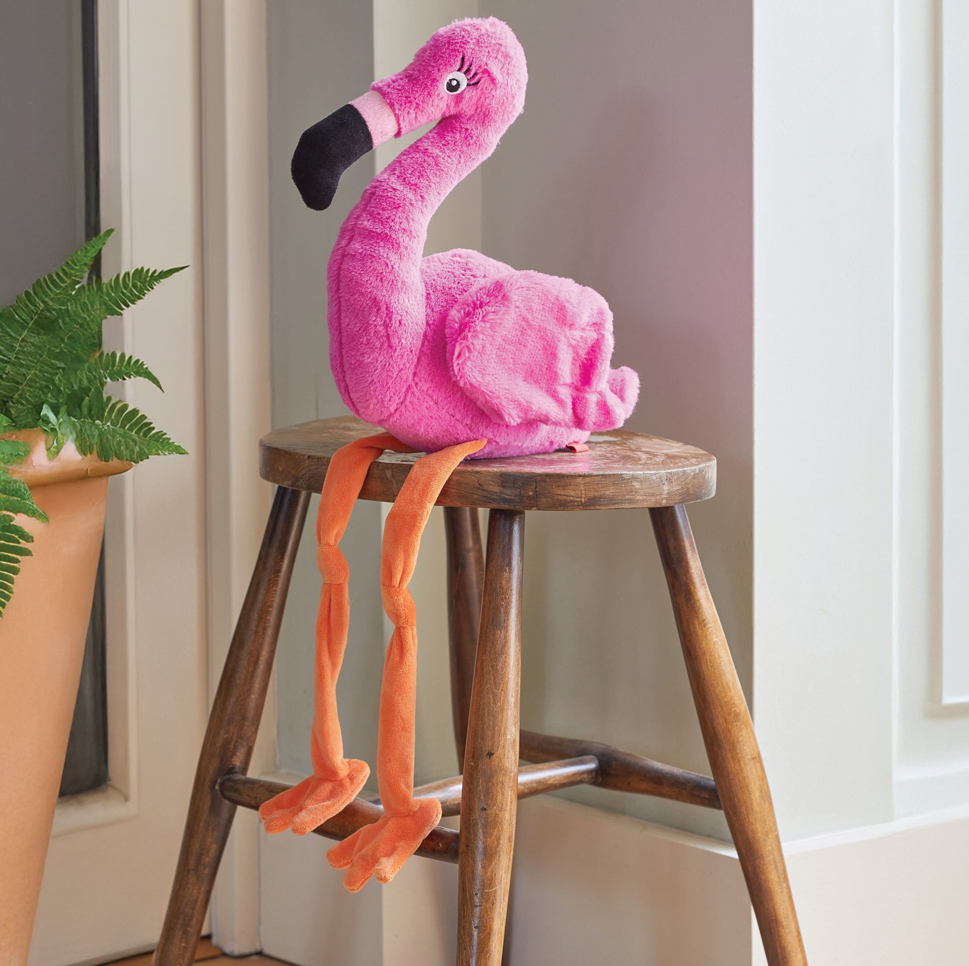 Pink plush flamingo toy on a wooden stool with a plant in the background