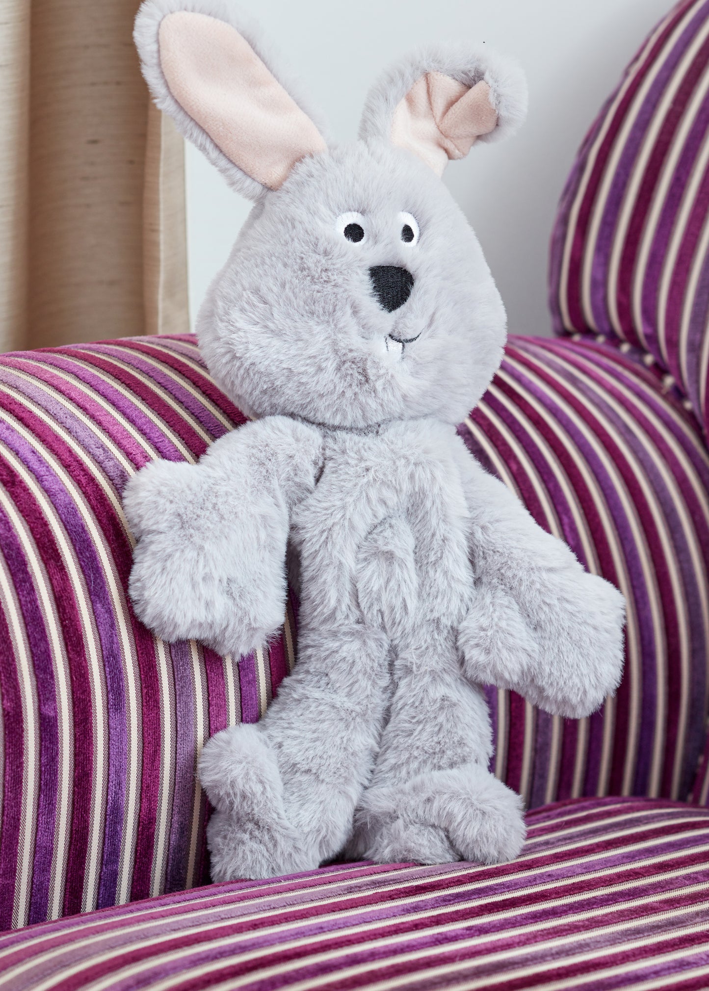 Gray plush bunny toy on a striped couch