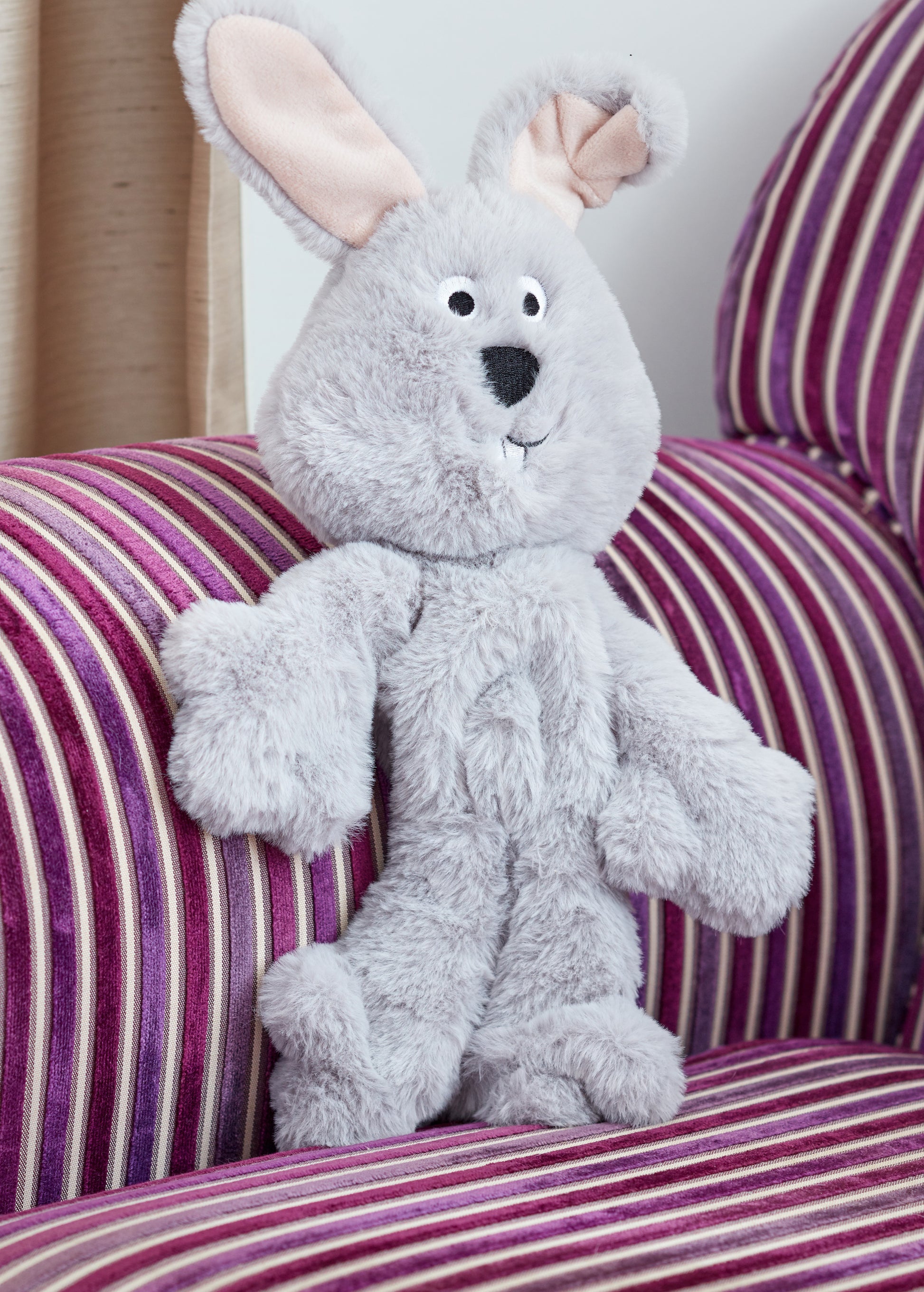 Gray plush bunny toy on a striped couch