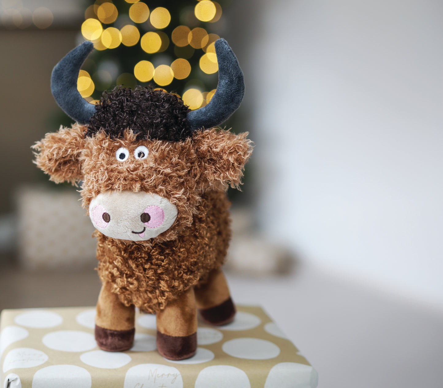 Plush toy cow with blue horns on a polka dot box with blurred lights in the background