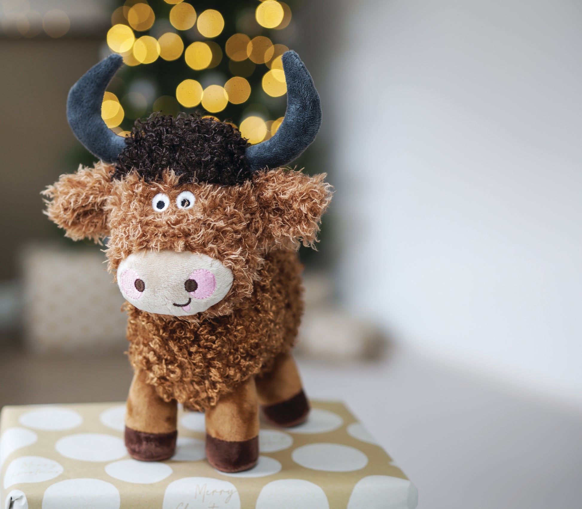 Plush toy cow with blue horns on a polka dot box with blurred lights in the background